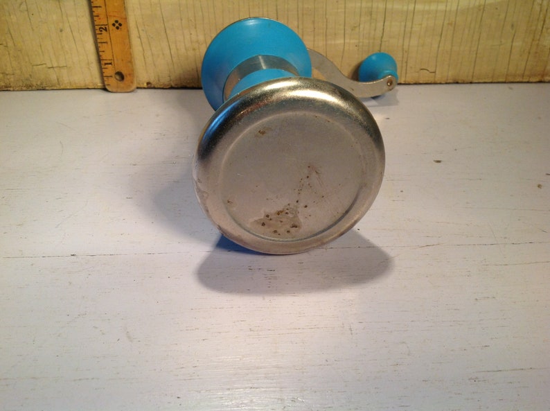 May include: A blue and silver hand-crank food grinder. The grinder has a round base and a crank handle.