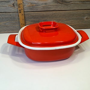 Pode incluir: Caçarola de esmalte vermelho com borda branca e tampa. A tampa tem uma pequena pega quadrada branca.