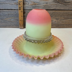 May include: A vintage glass lamp shade with a pink and yellow gradient. The shade has a ruffled edge and a decorative beaded band. The lamp shade is likely from the early 20th century.