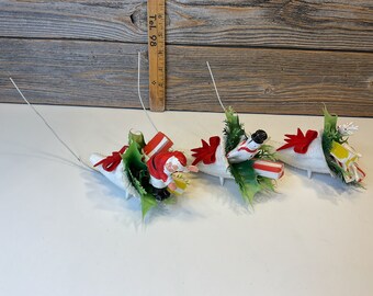 Könnte beinhalten: Drei weiße Füllhörner gefüllt mit Weihnachtsdekoration. Ein Füllhorn zeigt eine Weihnachtsmannfigur, ein anderes eine Schneemannfigur und das dritte eine Rentierfigur. Jedes Füllhorn ist mit roten Schleifen, grünem Stechpalmenlaub und Zuckerstangen verziert.