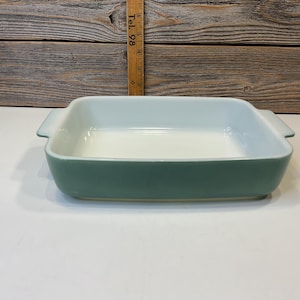 Puede incluir: Un molde para hornear de vidrio verde claro con interior blanco. El molde tiene dos asas a los lados.