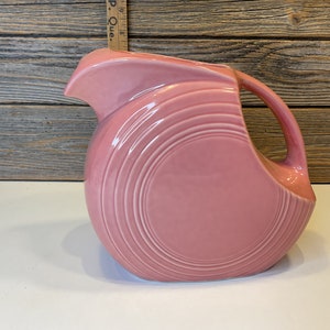 Peut inclure: Un pichet en céramique rose avec un corps arrondi et un bec large et évasé. Le pichet a un design nervuré et une poignée.