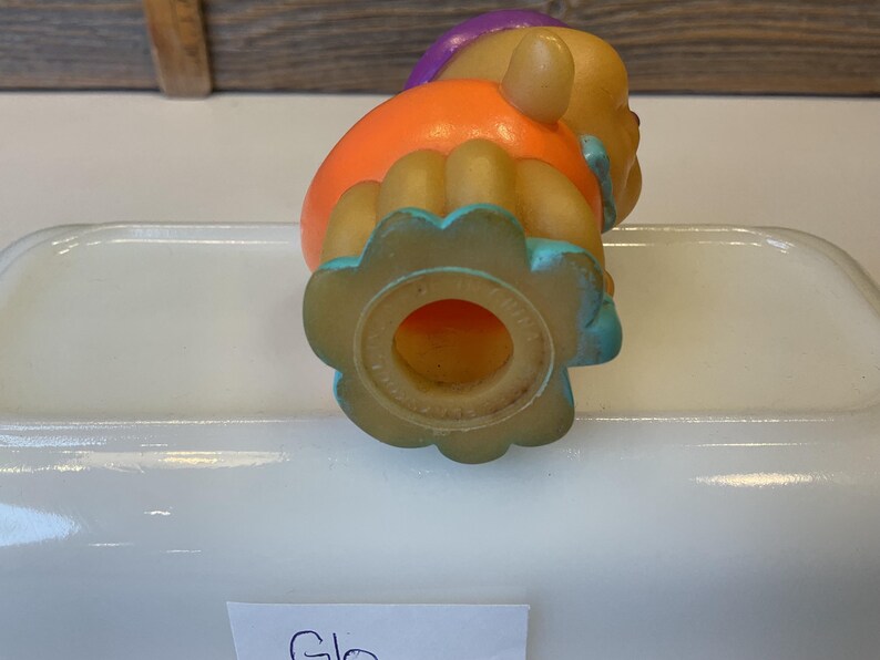 Puede incluir: Un juguete de goma colorido con un dise&ntilde;o morado, naranja y azul. El juguete tiene un agujero en la parte inferior y tiene forma de persona.