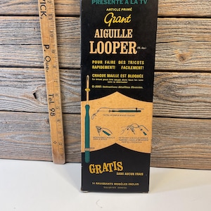 Peut inclure: Une boîte noire et jaune avec le texte "PRESENTE A LA TV" et "Grant AIGUILLE LOOPER (M. dep.)" sur le devant. La boîte contient une aiguille à tricoter en plastique verte avec une boucle métallique à l'extrémité. Le texte sur la boîte dit "POUR FAIRE DES TRICOTS RAPIDEMENT! FACILEMENT! CHAQUE MAILLE EST BLOQUÉE" et "GRATIS SANS AUCUN FRAIS".