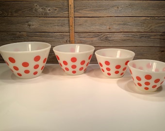 May include: Set of four white mixing bowls with a pink polka dot pattern. The bowls are arranged in order of size, with the largest bowl on the left and the smallest bowl on the right.