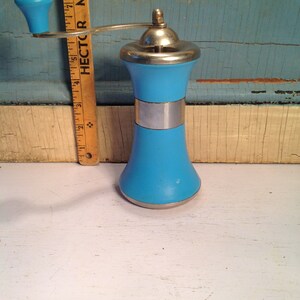 May include: A vintage blue and silver manual pepper grinder with a wooden handle. The grinder is on a white surface.