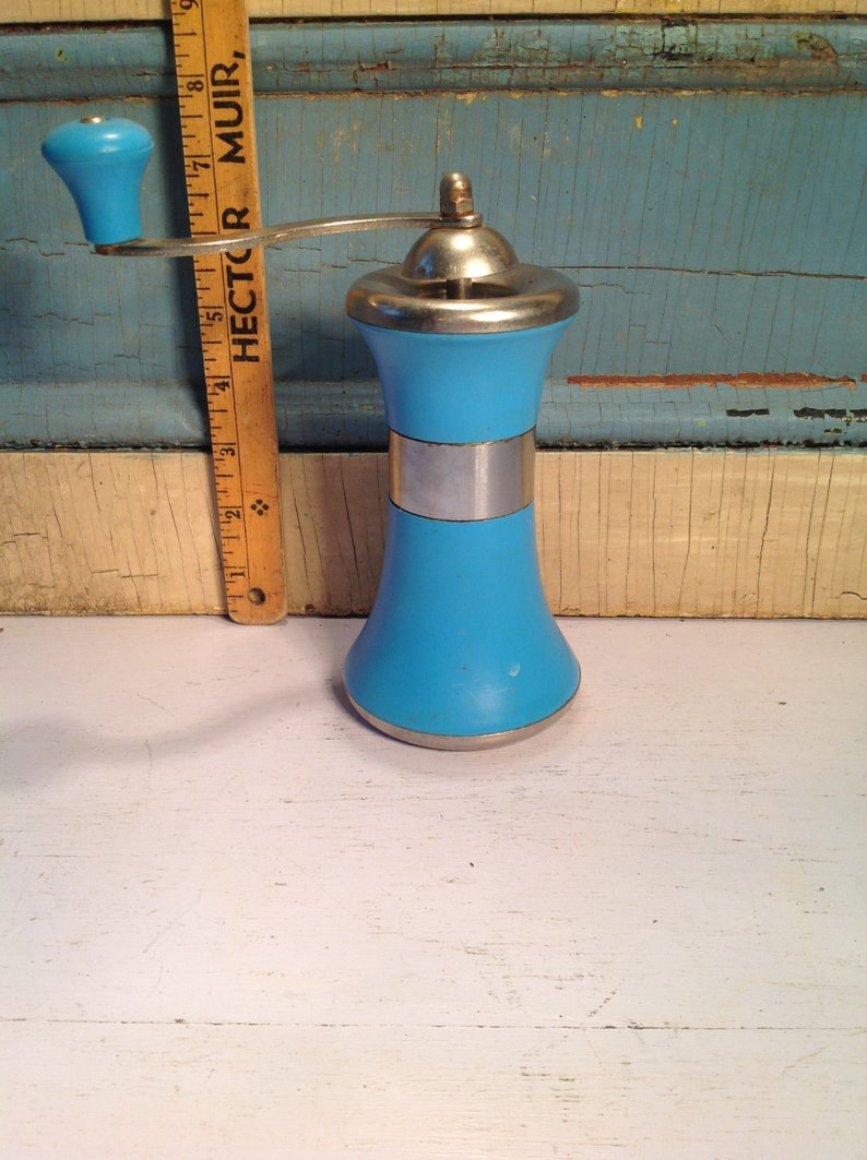 May include: A vintage blue and silver manual pepper grinder with a wooden handle. The grinder is on a white surface.
