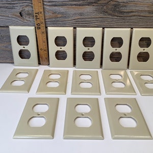 Puede incluir: Una colección de 12 tapas de tomacorriente de plástico de color crema.