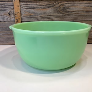 Peut inclure: Un grand bol à mélanger en verre vert pâle avec une surface lisse et arrondie. Le bol a une lèvre légèrement évasée et un fond arrondi.