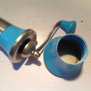 May include: A vintage blue and silver manual coffee grinder with a crank handle. The grinder has a removable blue plastic container for the coffee beans.