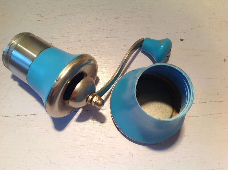 May include: A vintage blue and silver manual coffee grinder with a crank handle. The grinder has a removable blue plastic container for the coffee beans.