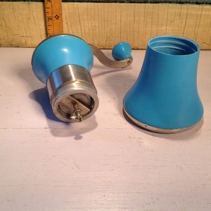 May include: A vintage blue manual coffee grinder with a silver base and a removable top. The grinder has a crank handle and a metal grinding mechanism.