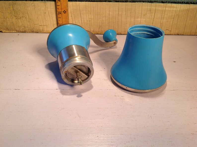 May include: A vintage blue manual coffee grinder with a silver base and a removable top. The grinder has a crank handle and a metal grinding mechanism.
