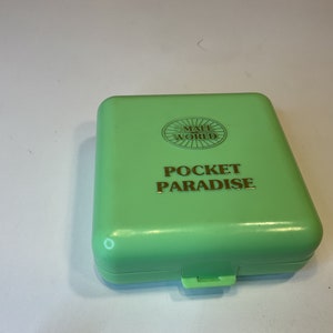 Op de afbeelding: Een groene plastic doos met de woorden "Small World" en "Pocket Paradise" erop gedrukt.