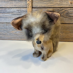 Peut inclure: Un jouet en peluche de renard vintage avec une fourrure brune, une tache blanche sur le front et des yeux noirs. Le jouet est debout sur une surface blanche.