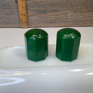 May include: Two green octagonal salt and pepper shakers on a white surface.
