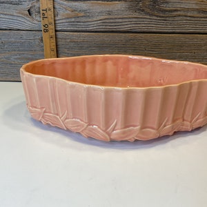 May include: A pale pink ceramic planter with a ribbed design and a leaf pattern around the rim.