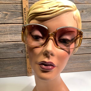 May include: A pair of large, brown, plastic framed sunglasses with white accents. The lenses are tinted a light brown color.