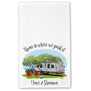 May include: A white kitchen towel with a colorful illustration of a camper parked in a campsite. The text "Home is where we park it" is written in a cursive font above the camper. The names "Dave & Shannon" are written below the camper.