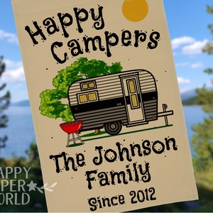 Thick, tan garden sized flag with vintage black and grey trailer in a campsite. Includes green trees, a bright yellow sun, and a red barbecue grill. 3 lines of customizable text under the graphic in a fun cartoon style font.