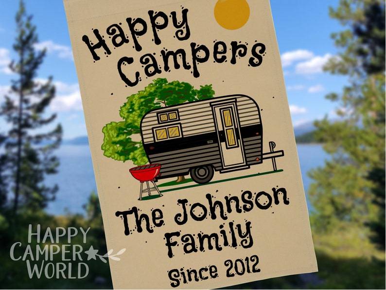 Thick, tan garden sized flag with vintage black and grey trailer in a campsite. Includes green trees, a bright yellow sun, and a red barbecue grill. 3 lines of customizable text under the graphic in a fun cartoon style font.