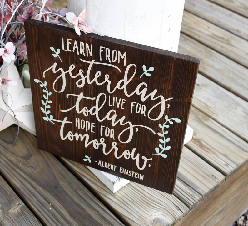 May include: A dark brown wooden sign with white and light blue lettering. The sign reads "Learn from yesterday, live for today, hope for tomorrow." - Albert Einstein.