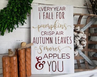 May include: White wooden sign with the text "Every year I fall for pumpkins, crisp air, autumn leaves, s'mores, apples & you" in gold and red lettering.