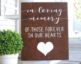 May include: A brown wooden sign with white lettering that reads "In loving memory of those forever in our hearts". A white heart is painted on the sign.
