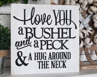 May include: White wooden sign with black text that reads "I love you a bushel and a peck & a hug around the neck."