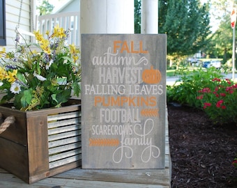 May include: A rustic wooden sign with the words "FALL, autumn, harvest, falling leaves, pumpkins, football, scarecrows, family" in orange and white paint.