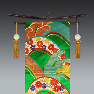 Può includere: Un rotolo appeso giapponese tradizionale con un design colorato di onde e fiori. Il rotolo è montato su un'asta di legno con nappe ad ogni estremità.