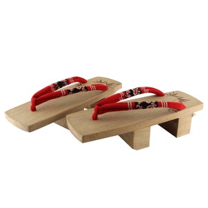 May include: A pair of wooden Japanese sandals, known as geta, with red fabric straps and a floral pattern. The sandals have a raised wooden base and are traditionally worn with a kimono.