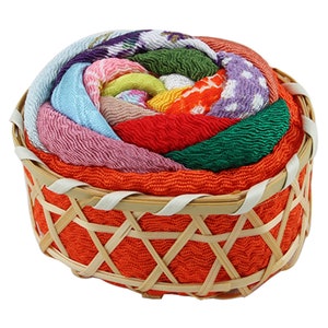 May include: A colorful assortment of fabric scraps arranged in a spiral pattern, resembling a flower, inside a woven orange bamboo basket.