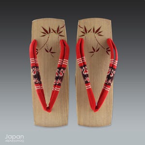 A very pretty pair of vintage Japanese geta. They are made of kiri (paulownia) wood which is a very light but strong wood. The wood is an unstained, natural color and there are lacquered brown bamboo leaves with a gold lacquer border on the heel. The interesting red, black and beige striped thongs with a small butterfly pattern make a great accent.