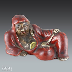 japanese antique ceramic daruma in red robe lying on side