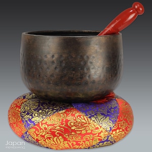 handcrafted vintage singing bowl on luxurious brocade cushion with striker