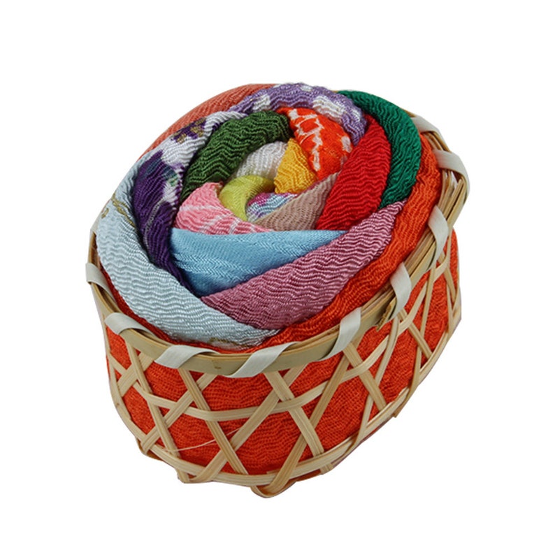 May include: A small, orange, woven basket filled with colorful fabric scraps arranged in a spiral pattern, resembling a rose.