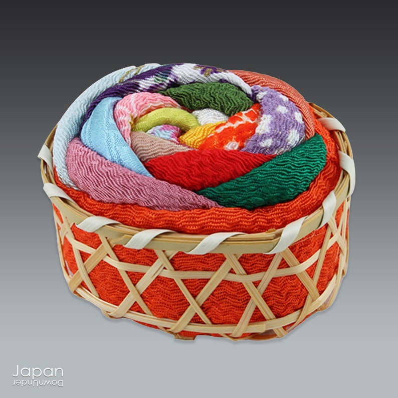 May include: A small, round, woven basket with a lid. The lid is made of colorful fabric, with a variety of patterns and colors, including pink, blue, green, yellow, and red. The basket is made of natural materials and has a traditional Japanese design.