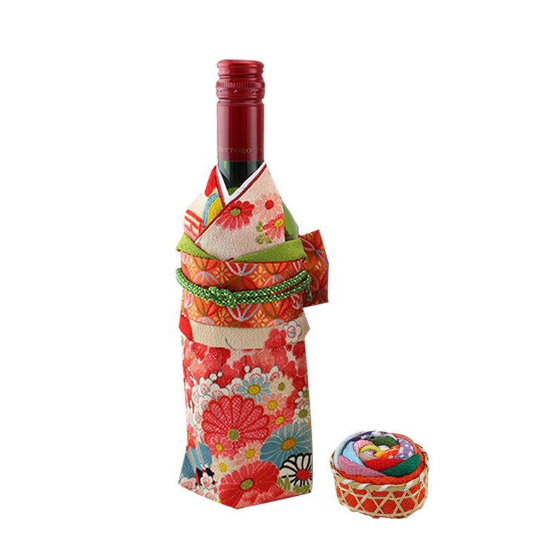 May include: A wine bottle wrapped in a colorful kimono-style fabric with a floral pattern. A small, round, fabric-covered box sits in front of the bottle.