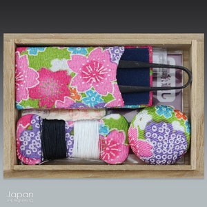 May include: A wooden box containing a sewing kit with floral patterned fabric, thread, and a pair of tweezers. The box is lined with a light brown fabric.