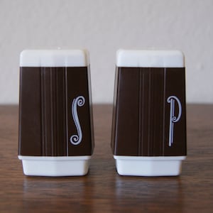 May include: A set of salt and pepper shakers. The shakers are brown with white tops and bases. The letters "S" and "P" are printed on the front in a white, stylized font. The brown section has vertical lines.