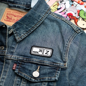 May include: A denim jacket with a black and white patch that reads "NOPE. ⌘ Z". The jacket has a classic design with a button closure and a Levi Strauss & Co. label.
