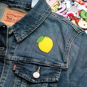 May include: A yellow lemon patch with green leaves sewn onto a blue denim jacket.