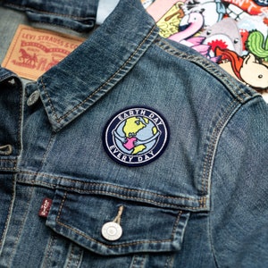 May include: A blue denim jacket with a patch that says "Earth Day Every Day" and features a cartoon image of a globe with two hands holding a heart.