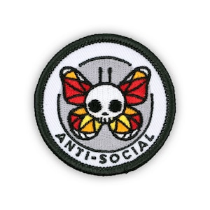 May include: A round black and white embroidered patch with a skull and butterfly design. The butterfly has red, orange, and yellow wings. The text "ANTI-SOCIAL" is written in black around the edge of the patch.