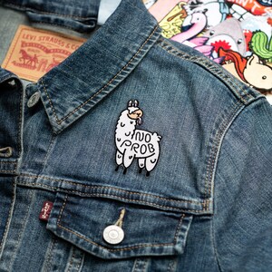 May include: A white embroidered patch of a llama with the text "no prob" on a denim jacket.