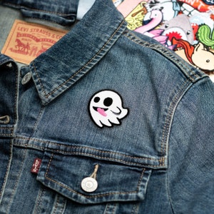 May include: A white ghost with a pink tongue sticking out, embroidered on a blue denim jacket.