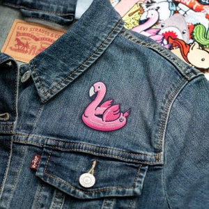 May include: A pink inflatable flamingo pool float patch sewn onto a blue denim jacket.