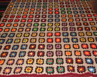 May include: A brown crocheted blanket with a repeating pattern of colorful squares. The squares are made with different colored yarn and have a flower-like design in the center.