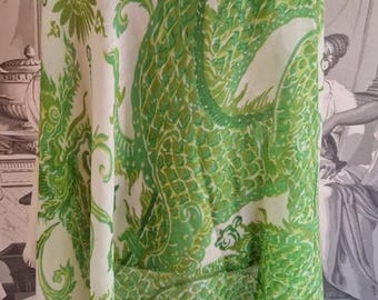 May include: A white scarf with a large green dragon design. The dragon is detailed with scales and curves, set against a backdrop of floral and abstract elements. The scarf is made of a lightweight fabric.